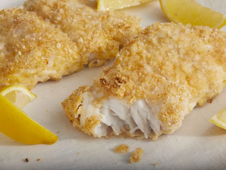 Golden crispy baked walleye fillets on a white plate, garnished with a slice of lemon and fresh herbs