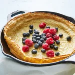 Golden Dutch Baby pancake fresh out of the oven, dusted with confectioners' sugar, served in a cast iron skillet