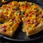 A freshly baked Eggs Benedict Breakfast Pizza on a wooden table, topped with creamy Hollandaise sauce, scrambled eggs, diced ham, and melted cheese