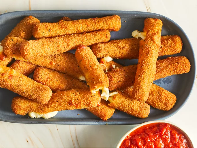 Golden fried mozzarella cheese sticks on a white plate, served with a bowl of marinara sauce for dipping