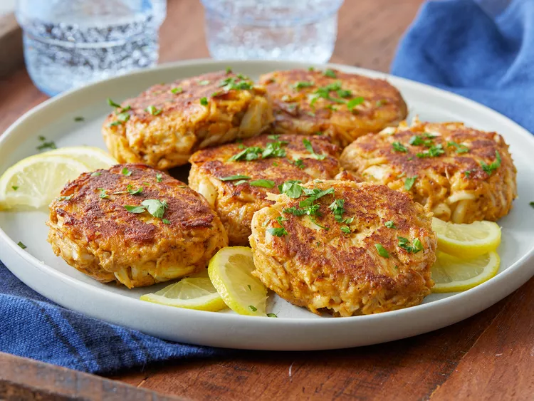 Golden brown Maryland crab cakes on a white plate, garnished with a slice of lemon and fresh parsley