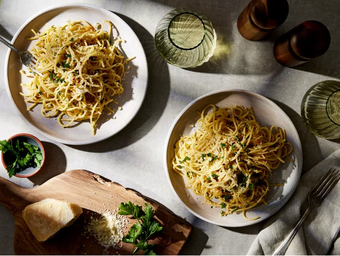 Plate of Spaghetti Aglio e Olio garnished with parsley and sprinkled with Parmigiano-Reggiano cheese, served on a rustic wooden table