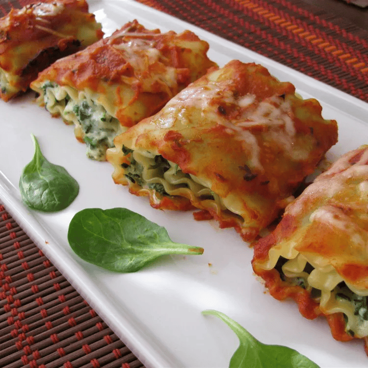 Freshly baked spinach lasagna rolls topped with melted mozzarella and served in a ceramic dish