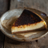 Slice of homemade burnt Basque cheesecake on a rustic ceramic plate with parchment paper, photographed in natural light on a wooden table.