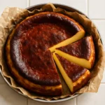 Overhead view of a burnt Basque cheesecake with a caramelized top and two slices pulled out, resting on parchment paper.